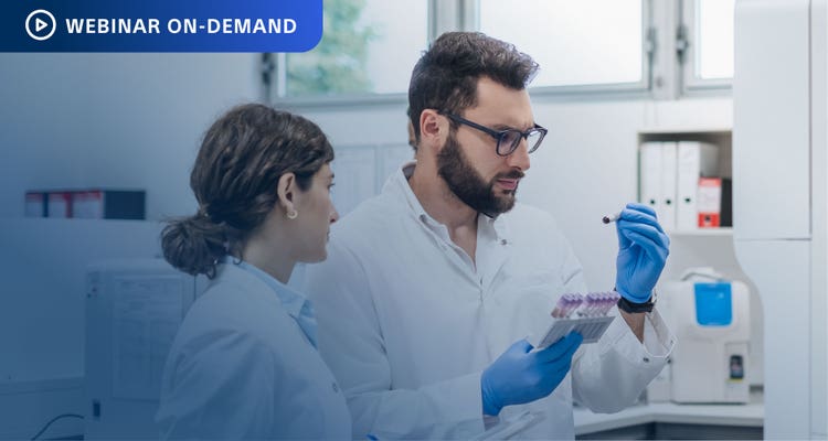 Two researchers in a lab setting, one is holding a tray of test tubes in one hand and a single test tube that both are looking at in the other.