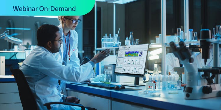 Webinar On-Deman. Two researchers in a dark lab looking at flow cytometry data on a computer display.
