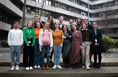 Photo of a group of people with a office buiding in the background.